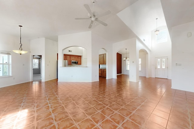 unfurnished living room with ceiling fan with notable chandelier, light tile patterned floors, and a high ceiling