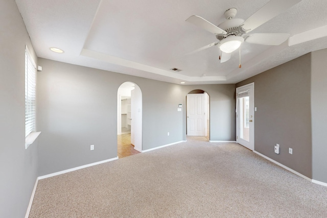 spare room with a raised ceiling, ceiling fan, and light carpet