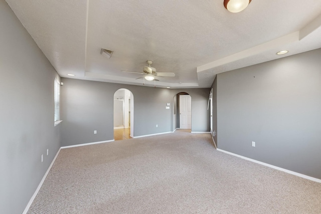 carpeted spare room with a textured ceiling, a tray ceiling, and ceiling fan