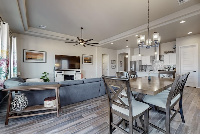 dining area with ceiling fan with notable chandelier, sink, and a tray ceiling