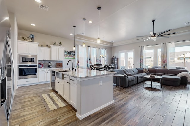 kitchen with light stone countertops, white cabinetry, sink, stainless steel appliances, and a center island with sink