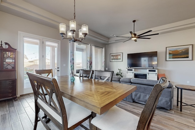 dining space featuring ceiling fan with notable chandelier, a tray ceiling, light hardwood / wood-style flooring, and plenty of natural light