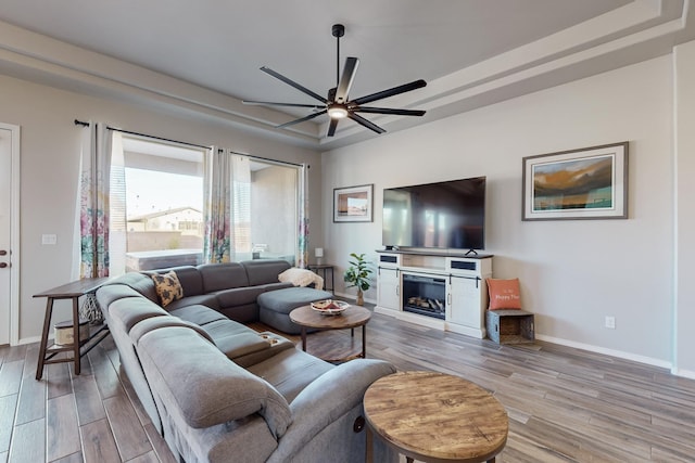 living room with a tray ceiling, light hardwood / wood-style flooring, and ceiling fan