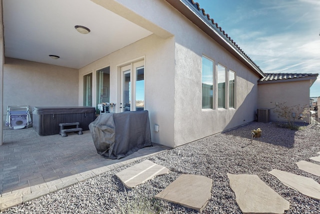 view of side of property with cooling unit, a patio, and a hot tub