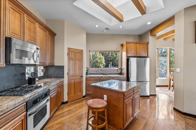 kitchen featuring appliances with stainless steel finishes, light wood-type flooring, tasteful backsplash, beamed ceiling, and a kitchen island