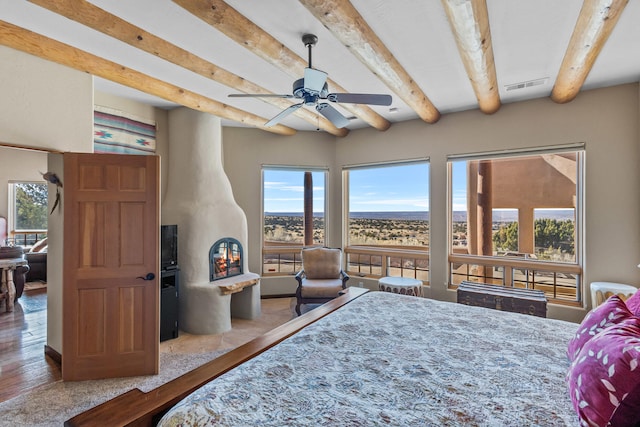 bedroom featuring beam ceiling, a large fireplace, and ceiling fan