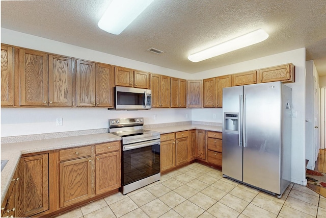 kitchen with light tile patterned flooring, stainless steel appliances, and a textured ceiling