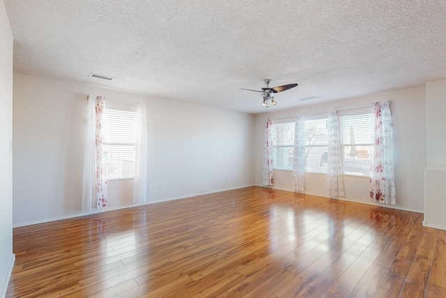 unfurnished room featuring a healthy amount of sunlight, ceiling fan, wood-type flooring, and a textured ceiling