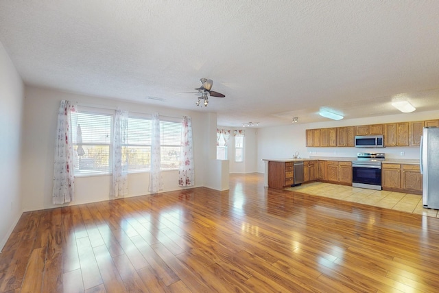 kitchen featuring kitchen peninsula, a textured ceiling, stainless steel appliances, ceiling fan, and light hardwood / wood-style flooring