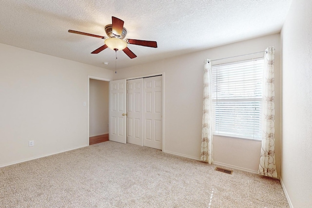 unfurnished bedroom featuring ceiling fan, a closet, light colored carpet, and a textured ceiling