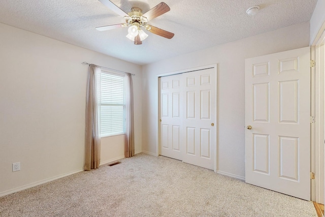 unfurnished bedroom featuring ceiling fan, a closet, light carpet, and a textured ceiling