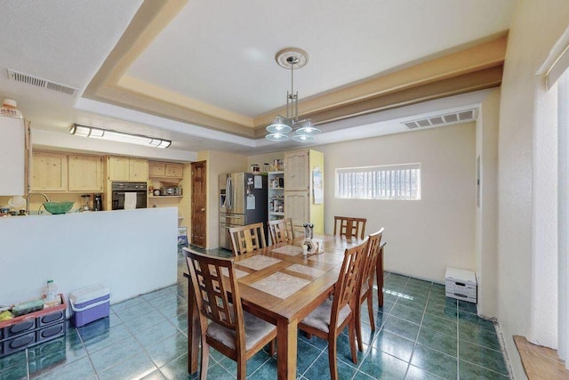 dining room featuring a tray ceiling, sink, and a chandelier