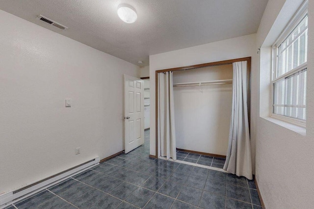 unfurnished bedroom featuring a textured ceiling, a closet, and baseboard heating