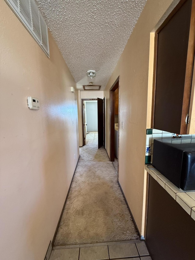 hallway featuring light carpet, visible vents, a textured ceiling, and light tile patterned floors