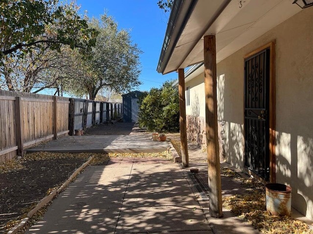 view of side of home featuring stucco siding, a storage shed, a fenced backyard, an outbuilding, and a patio