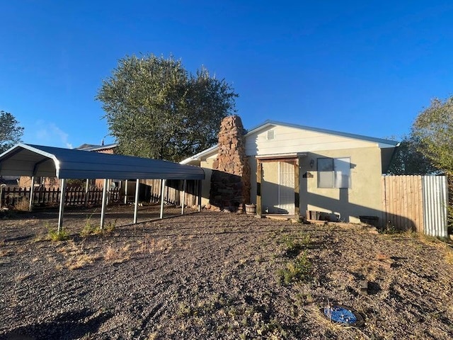 back of house with a carport, stucco siding, a chimney, and fence