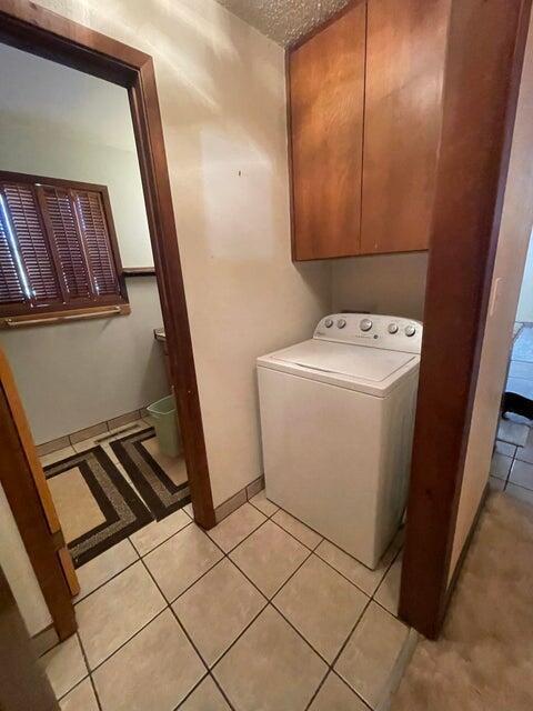 laundry area featuring light tile patterned floors, baseboards, washer / clothes dryer, cabinet space, and a textured ceiling