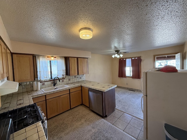 kitchen featuring a sink, range with gas cooktop, a peninsula, freestanding refrigerator, and stainless steel dishwasher