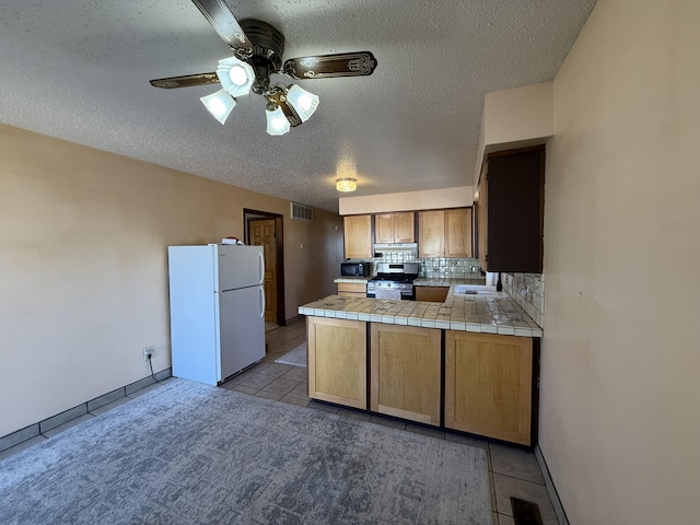 kitchen with stainless steel gas range oven, visible vents, black microwave, a peninsula, and freestanding refrigerator