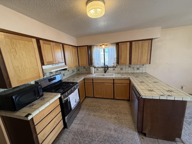 kitchen with stainless steel gas range oven, black microwave, tile counters, under cabinet range hood, and a sink