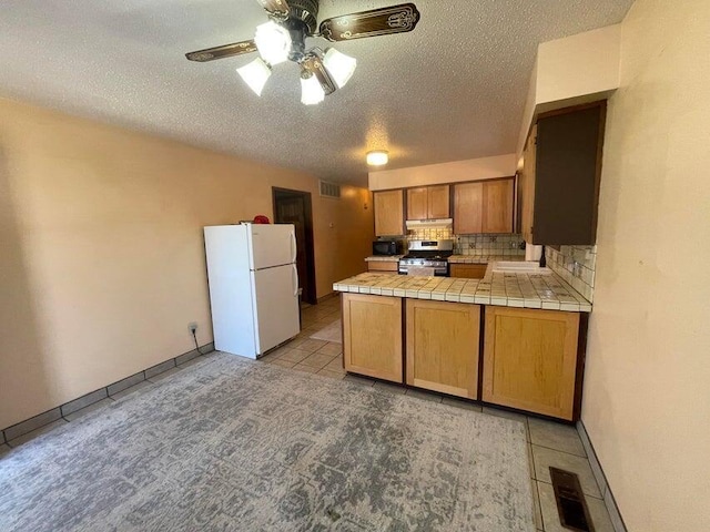 kitchen with visible vents, tasteful backsplash, freestanding refrigerator, a peninsula, and stainless steel gas range