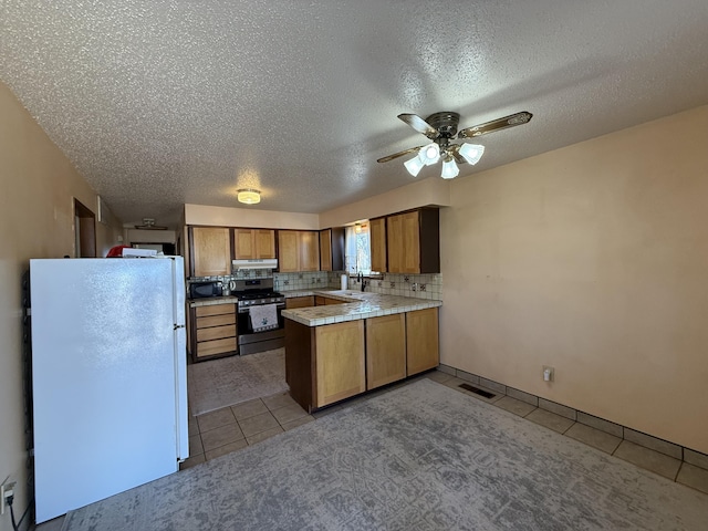 kitchen with stainless steel range with gas cooktop, black microwave, a peninsula, freestanding refrigerator, and brown cabinetry