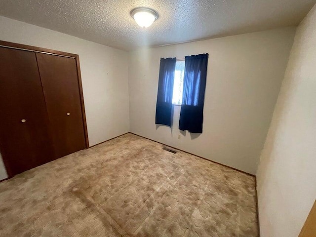 unfurnished bedroom with a closet, a textured ceiling, visible vents, and carpet