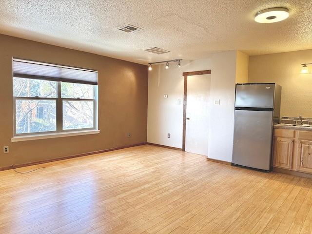 unfurnished room with a textured ceiling, track lighting, sink, and light hardwood / wood-style flooring