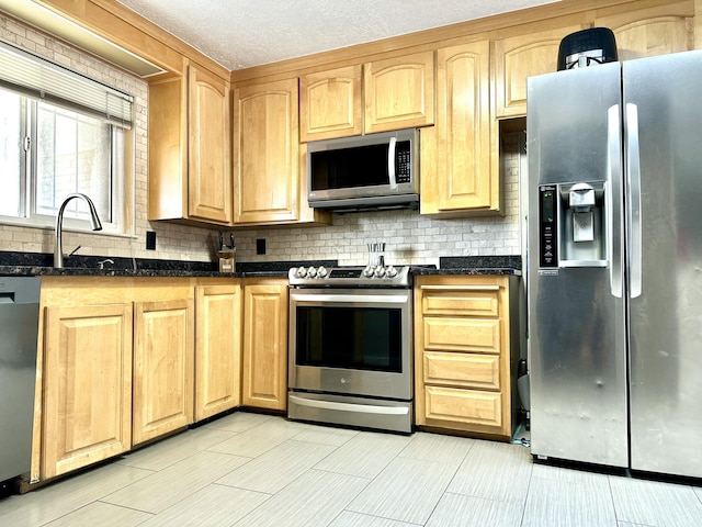 kitchen with decorative backsplash, appliances with stainless steel finishes, dark stone countertops, a textured ceiling, and a sink