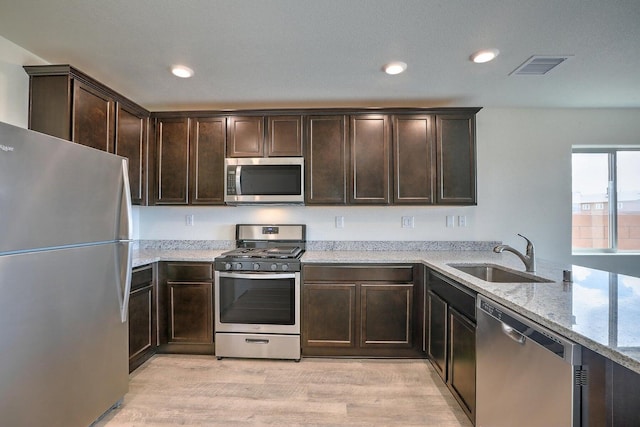 kitchen with sink, light hardwood / wood-style flooring, appliances with stainless steel finishes, dark brown cabinets, and light stone counters