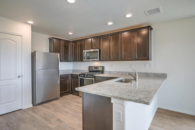 kitchen featuring sink, appliances with stainless steel finishes, light stone counters, kitchen peninsula, and light wood-type flooring