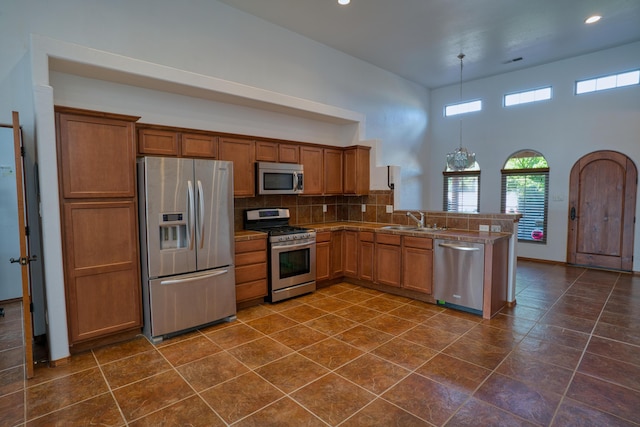 kitchen with appliances with stainless steel finishes, tasteful backsplash, sink, hanging light fixtures, and kitchen peninsula