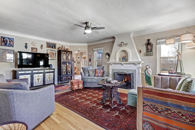 living room with hardwood / wood-style floors, ceiling fan, a textured ceiling, and a brick fireplace