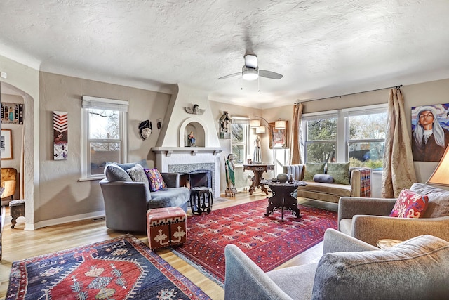 living room with a tile fireplace, ceiling fan, plenty of natural light, and wood-type flooring