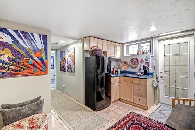 kitchen with black fridge, light brown cabinets, light tile patterned floors, and a textured ceiling