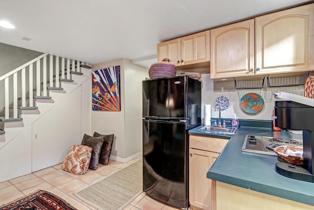 kitchen featuring stainless steel stovetop, black fridge, sink, light tile patterned floors, and light brown cabinetry