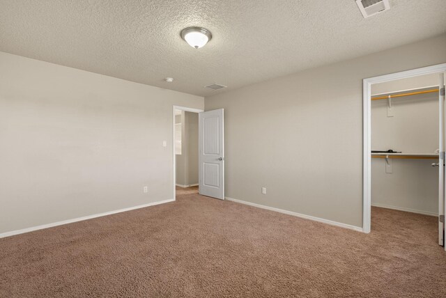 unfurnished bedroom featuring carpet, a textured ceiling, a walk in closet, and a closet