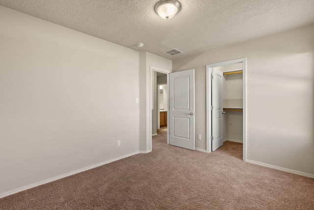 unfurnished bedroom featuring light colored carpet, a walk in closet, a textured ceiling, and a closet