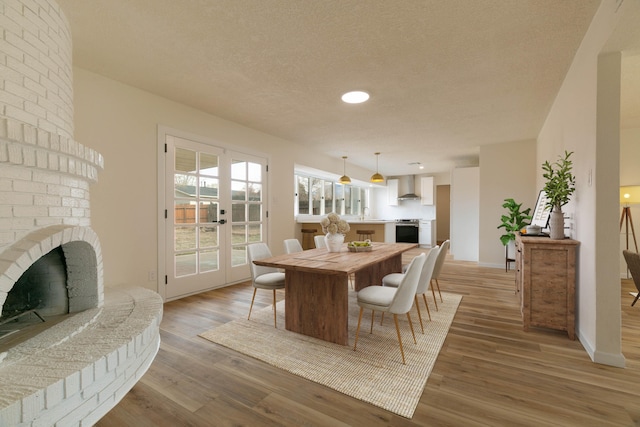 dining area with hardwood / wood-style flooring, a brick fireplace, french doors, and a textured ceiling