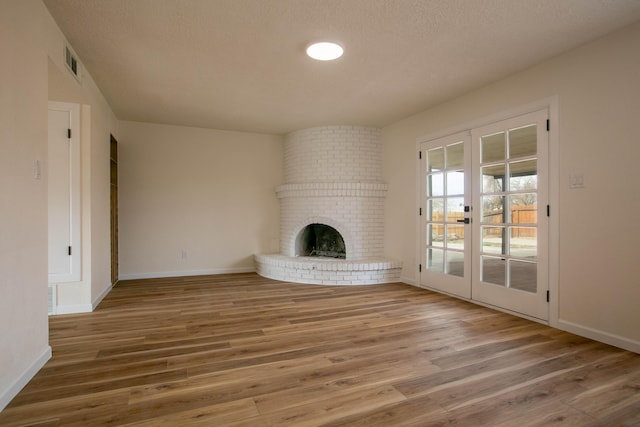 unfurnished living room featuring hardwood / wood-style flooring, a fireplace, a textured ceiling, and french doors