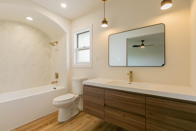 full bathroom with tiled shower / bath, hardwood / wood-style floors, vanity, ceiling fan, and toilet