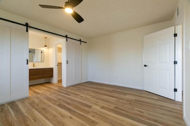 unfurnished bedroom with a barn door, connected bathroom, ceiling fan, and light hardwood / wood-style flooring