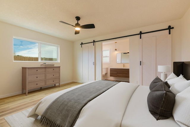 bedroom with ceiling fan, ensuite bath, a barn door, and light hardwood / wood-style flooring