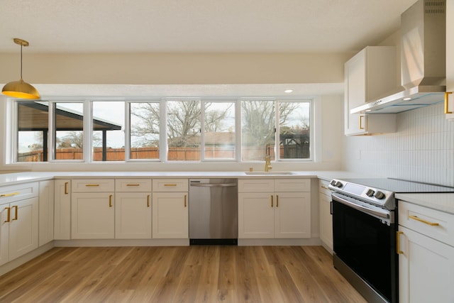 kitchen with pendant lighting, white cabinetry, sink, stainless steel appliances, and wall chimney exhaust hood