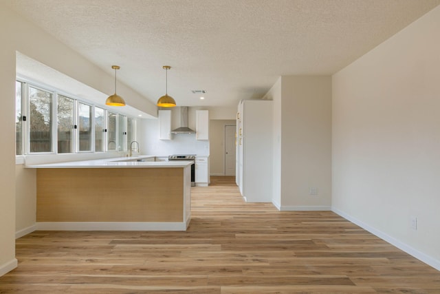 kitchen featuring electric range, decorative light fixtures, kitchen peninsula, wall chimney exhaust hood, and light wood-type flooring