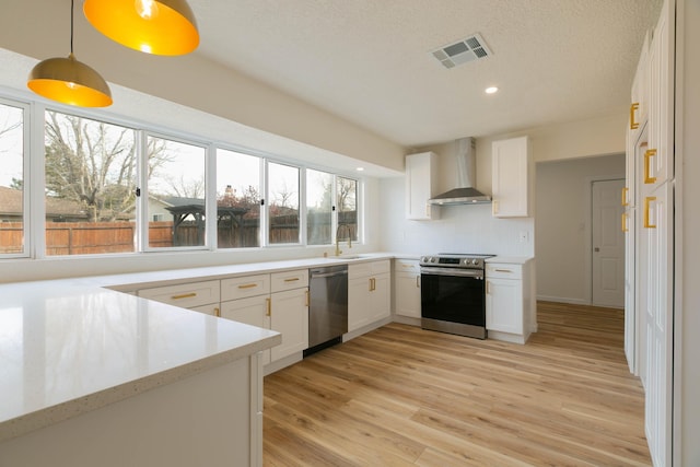 kitchen featuring white cabinetry, pendant lighting, stainless steel appliances, and wall chimney range hood