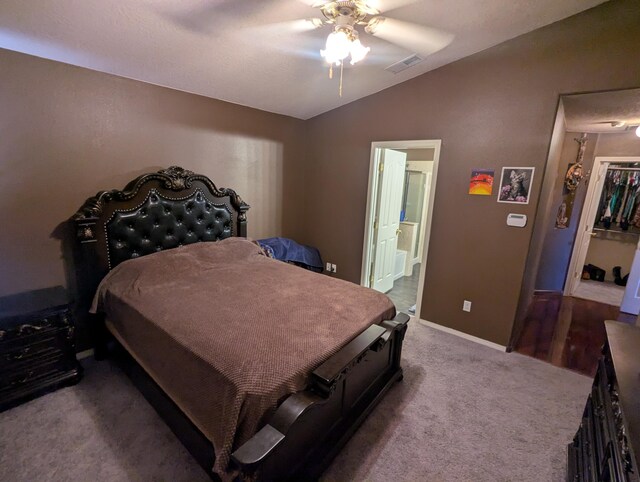 carpeted bedroom featuring lofted ceiling, a walk in closet, ceiling fan, ensuite bath, and a closet