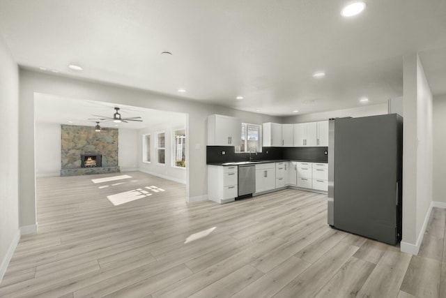 kitchen with stainless steel appliances, decorative backsplash, a fireplace, white cabinets, and sink