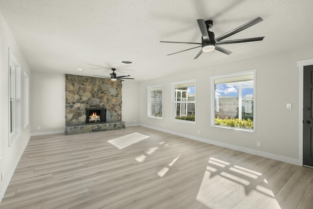 unfurnished living room with a textured ceiling, light hardwood / wood-style flooring, and a stone fireplace