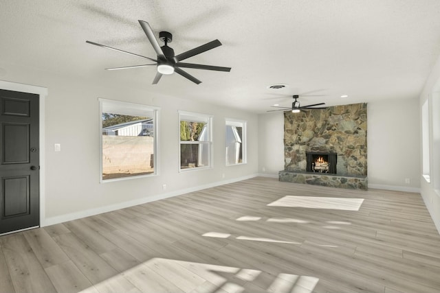 unfurnished living room with light hardwood / wood-style floors, a stone fireplace, and a textured ceiling